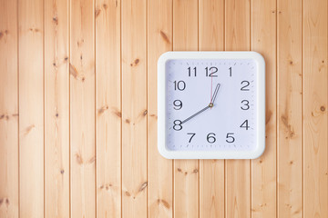 Square white clock on a wooden wall. Wooden background. The clock is shown at twenty in the morning.