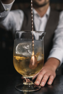 A vertical image of barman's hands stirring up a cocktail with ice cubes in a mixing glass.