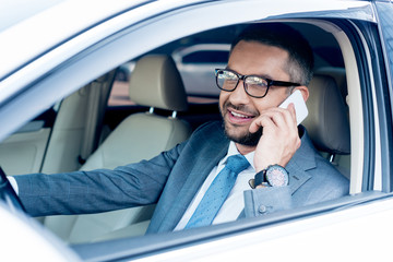 smiling businessman talking on smartphone while driving car