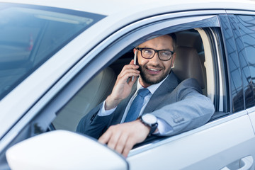 portrait of smiling businessman talking on smartphone while driving car