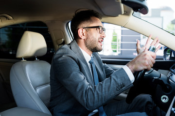 side view of emotional businessman in suit and eyeglasses driving car alone