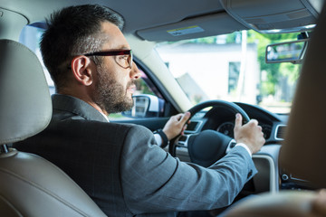 back view of businessman in suit and eyeglasses driving car alone