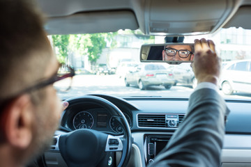 partial view of businessman in eyeglasses looking at rear view mirror in car