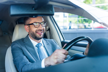 portrait of smiling businessman in suit and eyeglasses driving car alone