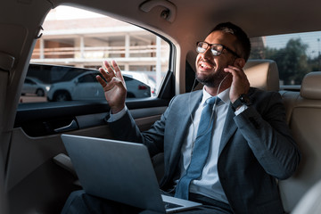 businessman in earphones with laptop listening music in car