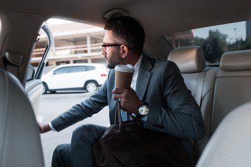 businessman with coffee to go sitting in car with opened door