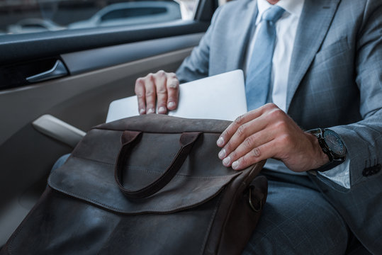 Cropped Shot Of Businessman In Suit Putting Papers Into Bag While Sitting On Backseat In Car