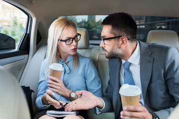 portrait of business people with coffee to go discussing work on back seats in car