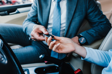 cropped shot of businessman giving car keys to colleague at driver seat in car