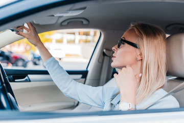 side view of blonde businesswoman in eyeglasses looking at rear view mirror in car