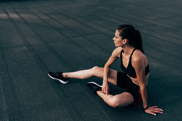 young athletic woman in sportswear sitting on asphalt