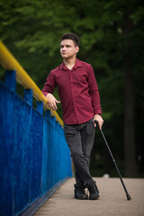 Young man standing on the bridge with a cane in his hand
