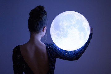 Elegant woman holding a big sphere glowing moon. Unrecognizable person, rear view
