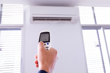 Air conditioner with remote controller,inside the room with man operating remote controller.