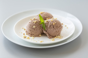 Tasty homemade bowl of chocolate ice cream with mint and nuts on a light background. 