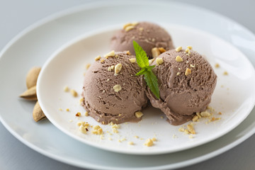 Tasty homemade bowl of chocolate ice cream with mint and nuts on a light background. 