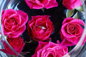 red buds of roses in a glass vase with water and a gold ring