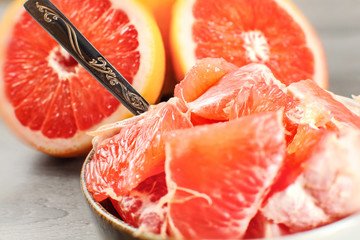 Detail photo - peeled grapefruit cut into pieces in small bowl with spoon, with whole citrus in background.