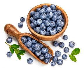 Berry blueberry in wooden dish with scoop and green leaves.