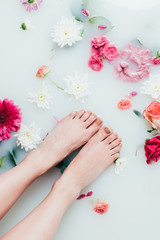 Obraz na płótnie Canvas partial view of female feet and beautiful colorful flowers in milk