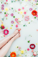 Fototapeta na wymiar cropped shot of female legs and various arranged beautiful flowers in milk