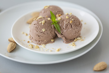 Tasty homemade bowl of chocolate ice cream with mint and nuts on a light background. 