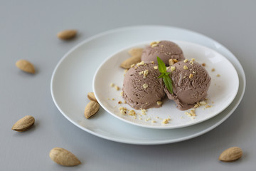 Tasty homemade bowl of chocolate ice cream with mint and nuts on a light background. 