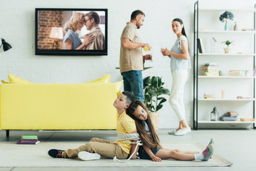 parents resting with champagne and kids sitting tied with rope on floor at home