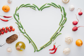 top view of heart made of fresh green peas and spices with ripe vegetables isolated on white