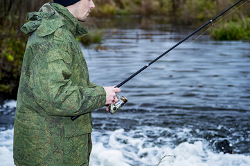 Male angler catches on a spinning reel the fish in fast water in the offseason.