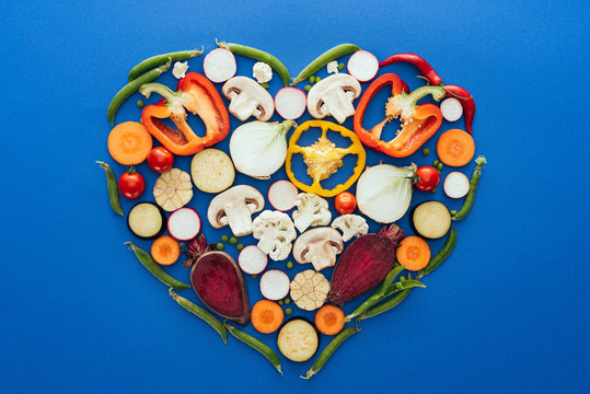 top view of various raw healthy vegetables in shape of heart isolated on blue