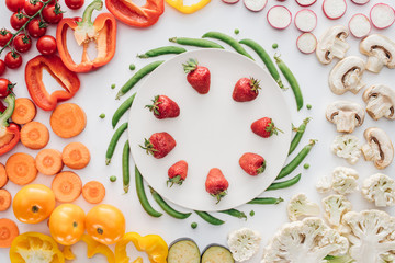 fresh ripe strawberries on round white plate and organic vegetables isolated on white