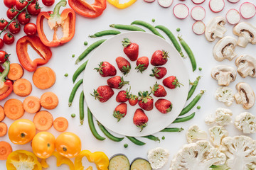 top view of fresh ripe strawberries on round white plate and organic vegetables isolated on white