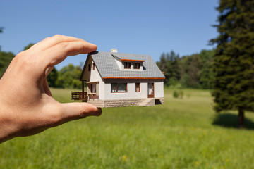 Dream to have a house. Hand holding a model house in green field - Powered by Adobe