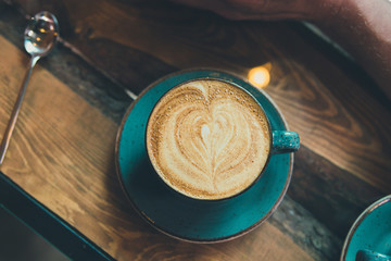 A green cup of cappuccino with a pattern in the shape of a heart, stands on a table in a cafe, top view.