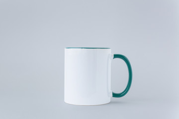 White mug with a greeen handle on a gray background.
