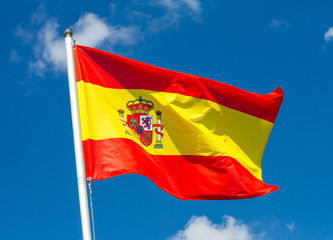 Flag of Spain waving in the wind on flagpole against the sky with clouds on sunny day, close-up