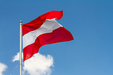 Flag of Austria waving in the wind on flagpole against the sky with clouds on sunny day, close-up