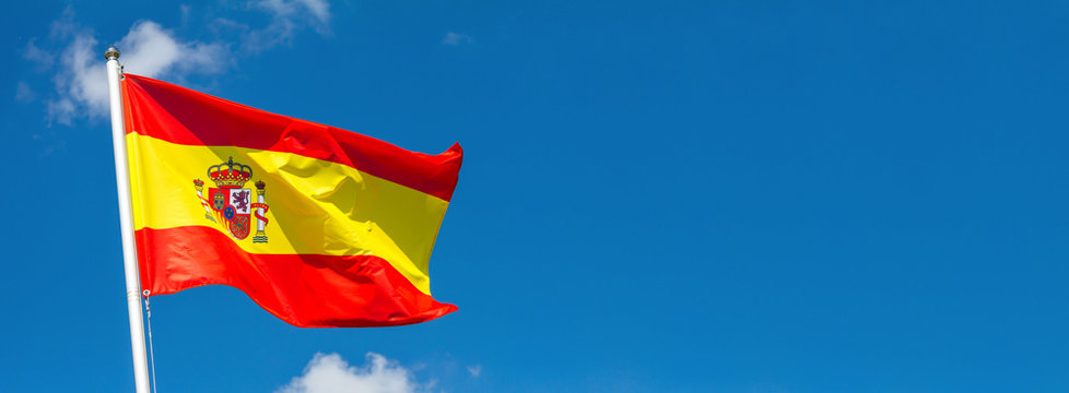 Flag of Spain waving in the wind on flagpole against the sky with clouds on sunny day, banner, close-up