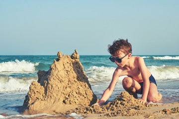 The child builds a sand castle from wet sand. A boy in sunglasses plays on the beach in toys on a...