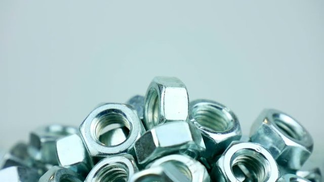 Stack of shiny nuts rotating on a mirror background. Pile of fastener with a threaded hole that forms a connection with a screw, bolt or stud
