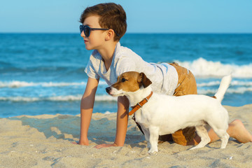 Happy boy hugging his dog breed Jack russell at the seashore against a blue sky close up at sunset. Best friends rest and have fun on vacation, play in the sand against the sea