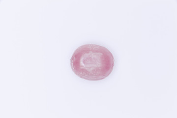 A hard sugar candy in the shape of an oval. Pink on white. Isolated studio shot.
