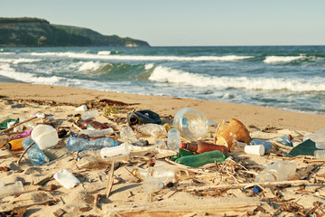 Spilled garbage on the beach of the big city. Empty used dirty plastic bottles. Dirty sea sandy shore the Black Sea. Environmental pollution. Ecological problem. Bokeh moving waves in the background  