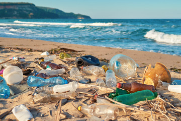 Spilled garbage on the beach of the big city. Empty used dirty plastic bottles. Dirty sea sandy shore the Black Sea. Environmental pollution. Ecological problem. Bokeh moving waves in the background  