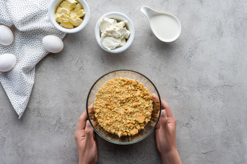 cropped shot of woman holding bowl with crushed cookies for pie on grey tabletop