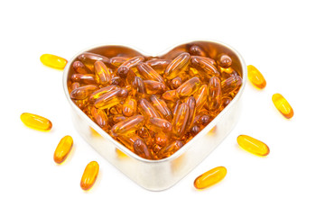 Fish oil capsules in a heart shape plate isolated on white background, vitamin D supplement, selective focus