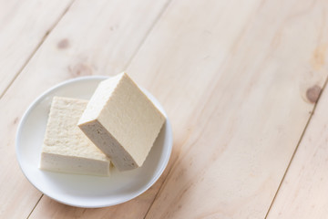 Tofu made from soybean on white plate over wooden background