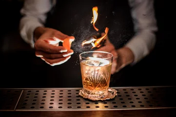 Foto op Aluminium Barman maakt een frisse en smakelijke ouderwetse cocktail met sinaasappelschil en rooknoot © fesenko