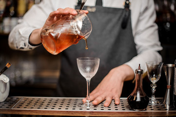 Bartender pouring fresh alcoholic drink into the cocktail glass